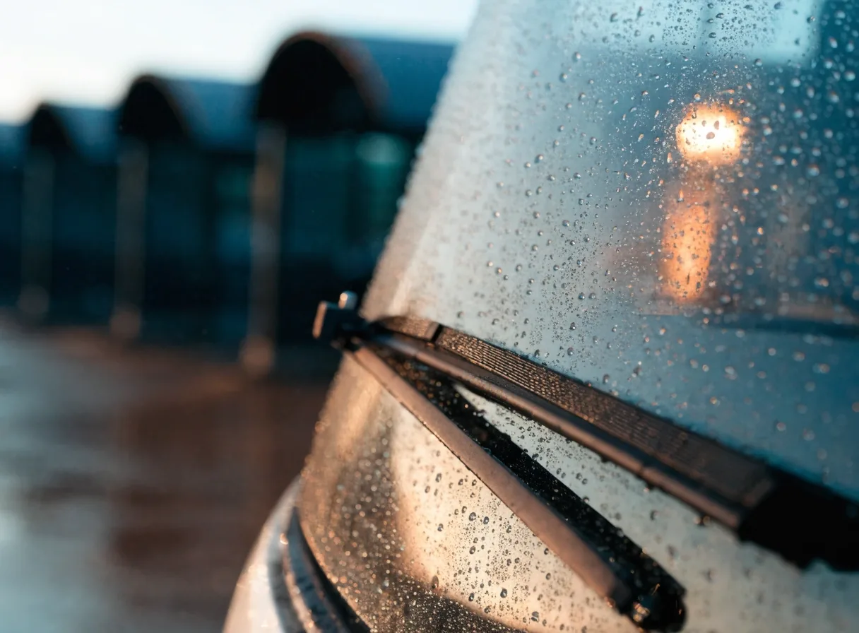 Rain beading on a shuttle windshield wiper blade at a car park stop in cold dawn light